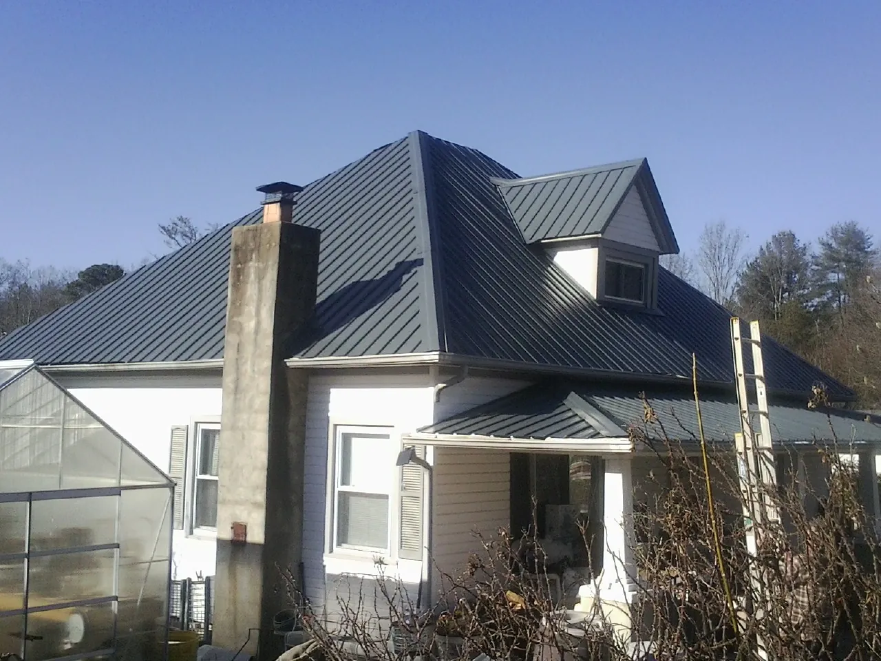 Dark blue standing seam metal roof on a white farmhouse with dormer — Slate & Tile Roof Repair by Roofing Brothers in Poplar Grove