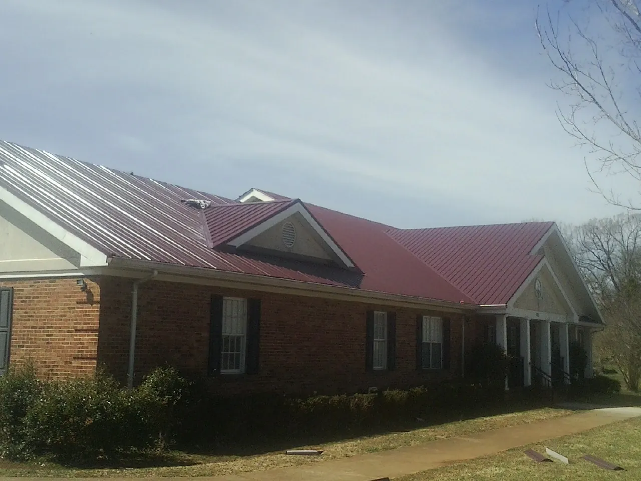 Red metal roof with gabled entries on a long brick building, from a Hail Damage Roof Repair job in Poplar Grove