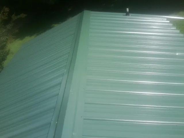 New green metal panels meeting at the ridge of a roof — Flat Roof Repair work by our crew in Poplar Grove
