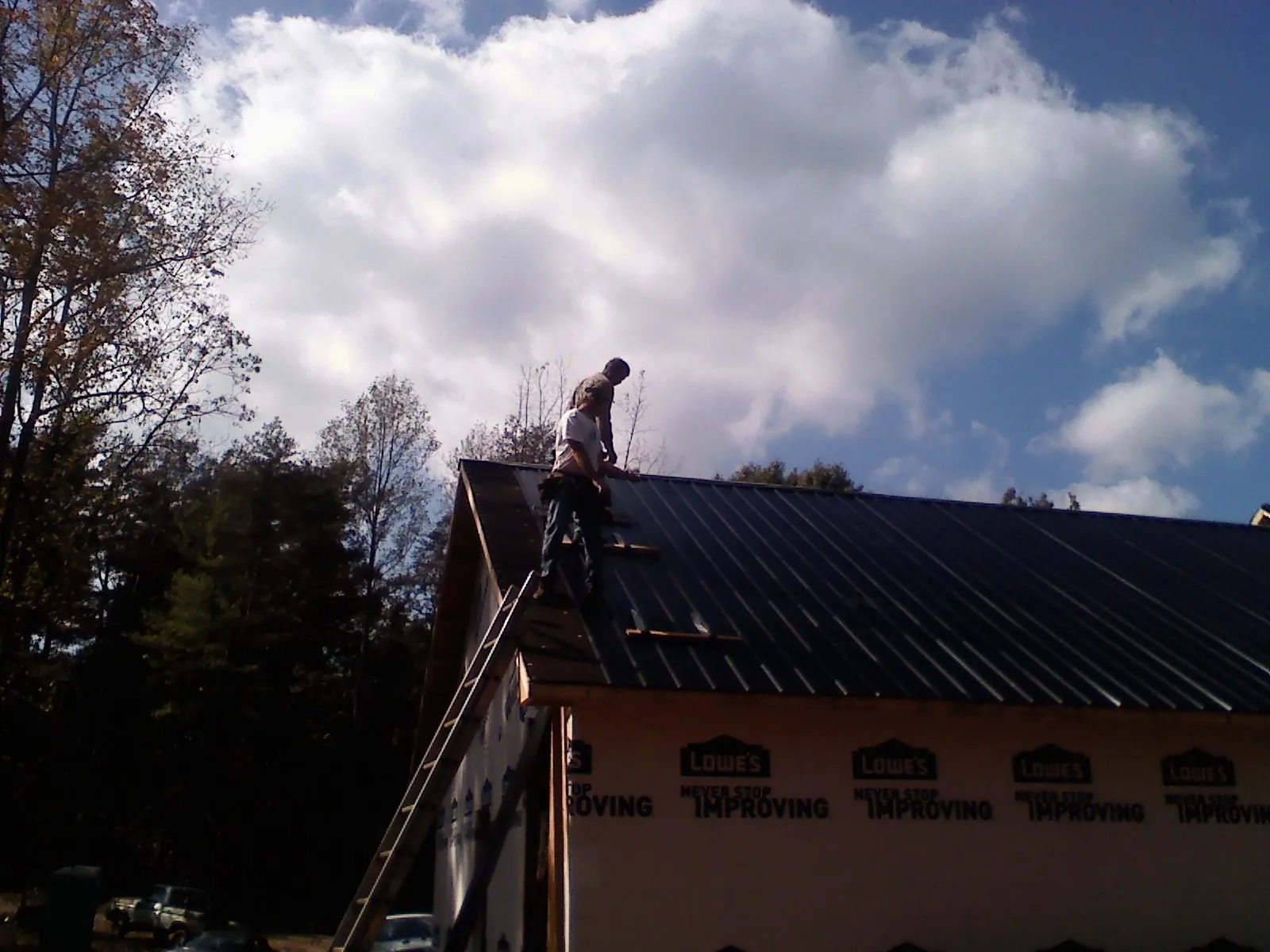 Roofer fastening dark metal panels high against a cloudy sky, from a Roof Inspection job in Poplar Grove