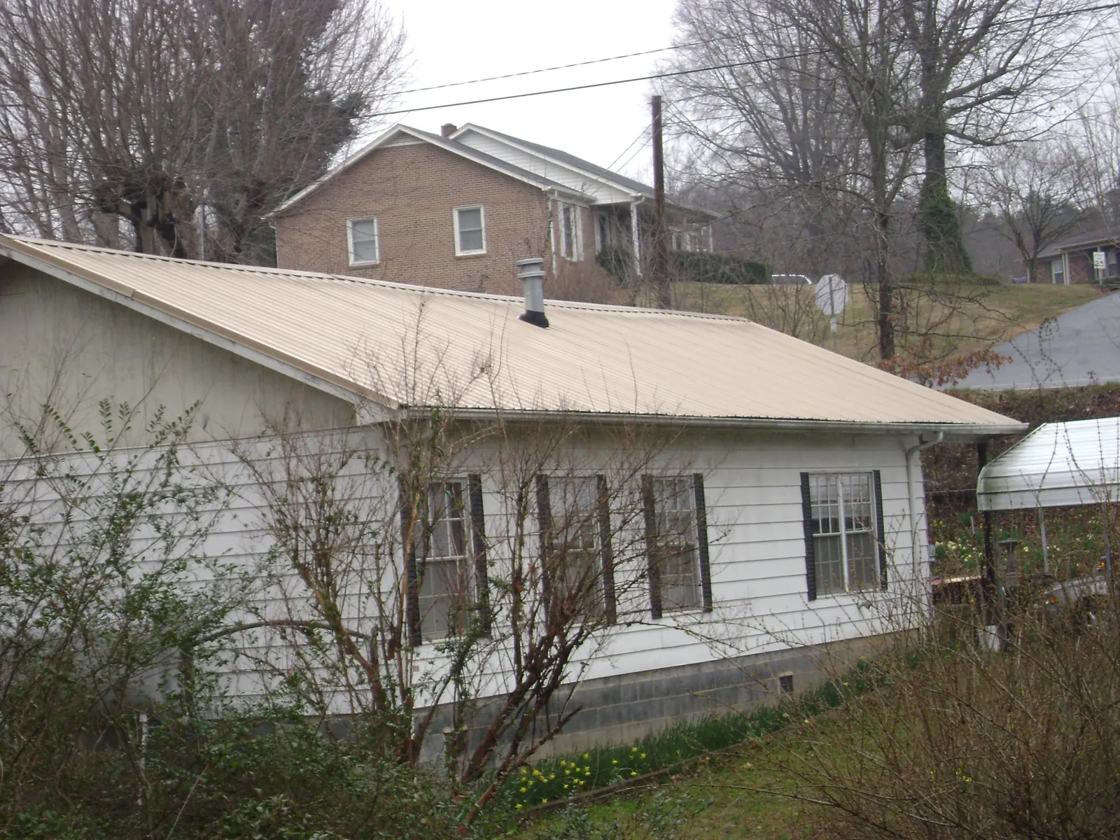 Tan metal roof on a white sided house set into a hillside — Commercial Roofing by Roofing Brothers in Poplar Grove