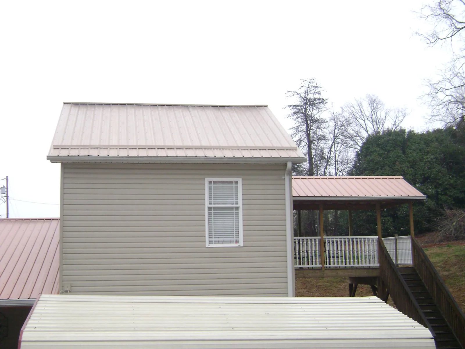 Tan metal roofs on a two story addition and attached porch, from a Roof Replacement job in Poplar Grove